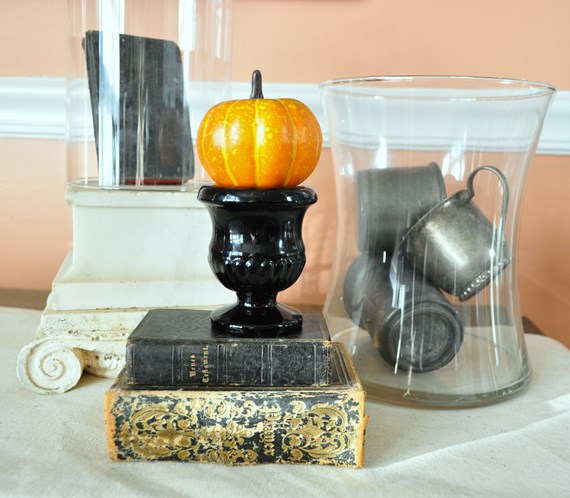 Tiny pumpkin on black glass match holder next to silver plate cups in a glass jar